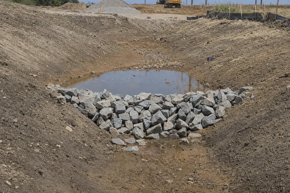 Rock check dam slowing water flow in a drainage channel